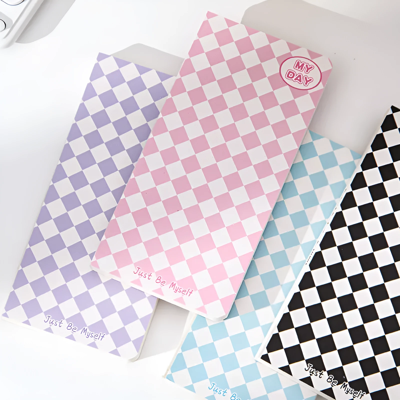 Ins style A5 grid notebook open on a desk, showing grid paper and one of twelve colourful cover designs like pineapple or checkerboard.